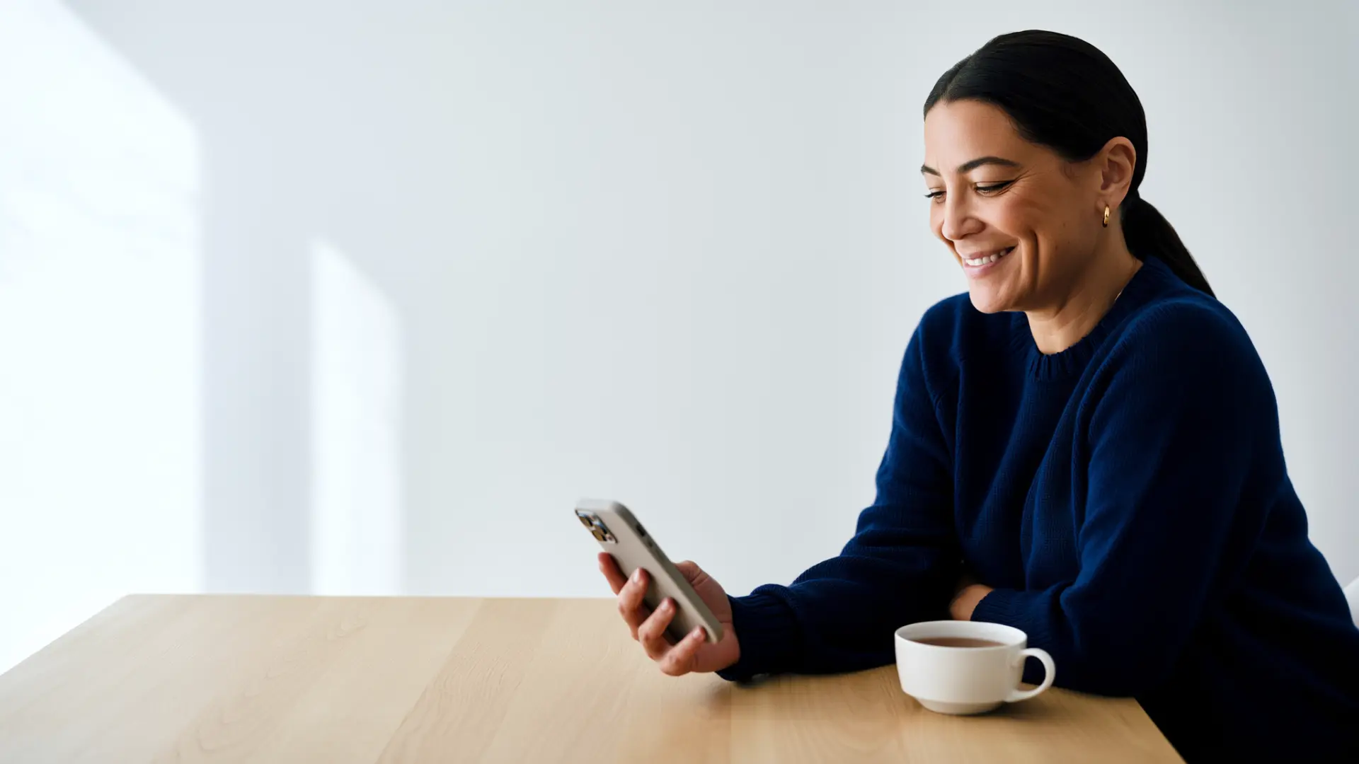 A woman at her kitchen table smiling as she reads her phone